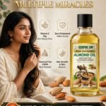 Seraphic Sun Wood-Cold Pressed Almond Oil bottle alongside a woman and raw almonds, highlighting product benefits including Vitamin E, zero cholesterol, and chemical-free slow pressing.